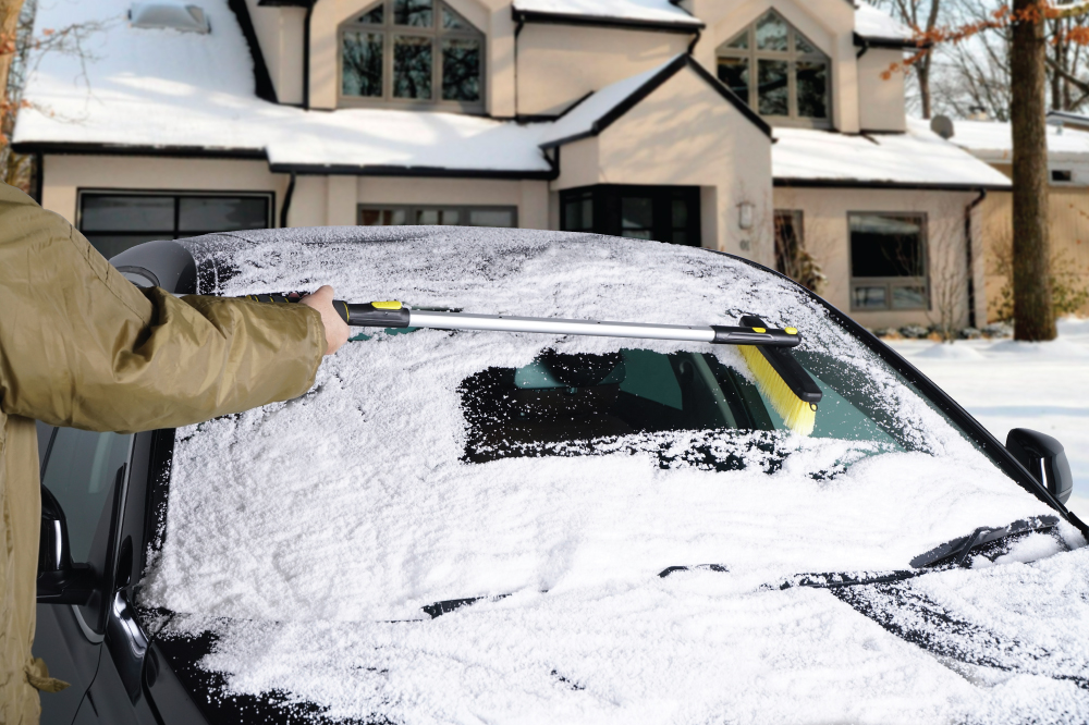 A man clearing snow on a car's wind shield using Power Brush & Scraper